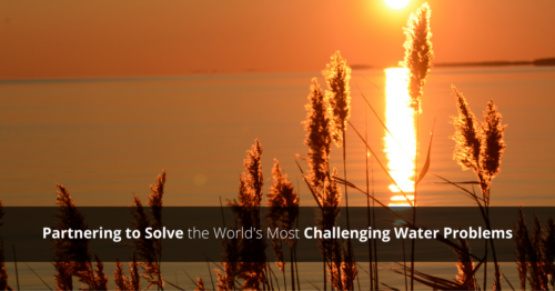 An orange sunset over the water with a text overlay that reads, "Partnering to Solve the Worlds Most Challenging Water Problems."